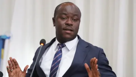 Water Minister Juma Aweso in a dark suit, white shirt and stripped tie, speaks to a microphone