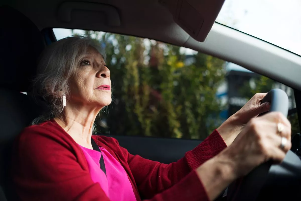 An elderly-white haired Mexican woman drives a car.