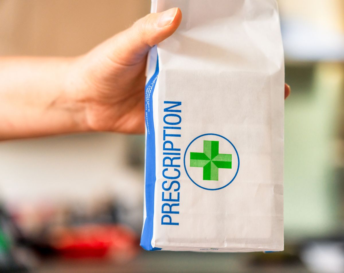 Close-up of a paper prescription bag, held out by a pharmacist.