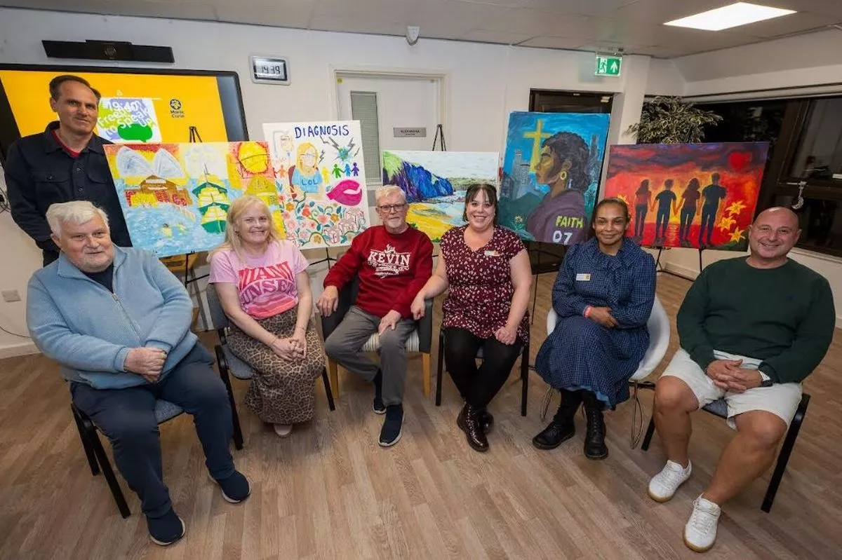 A group of people of mixed ages sitting in front of paintings on easels 