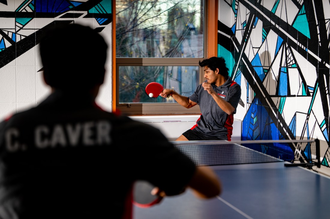 An action shot of Aditya Mitra and Caden Caver playing table tennis. Mitra is about to hit the ball.