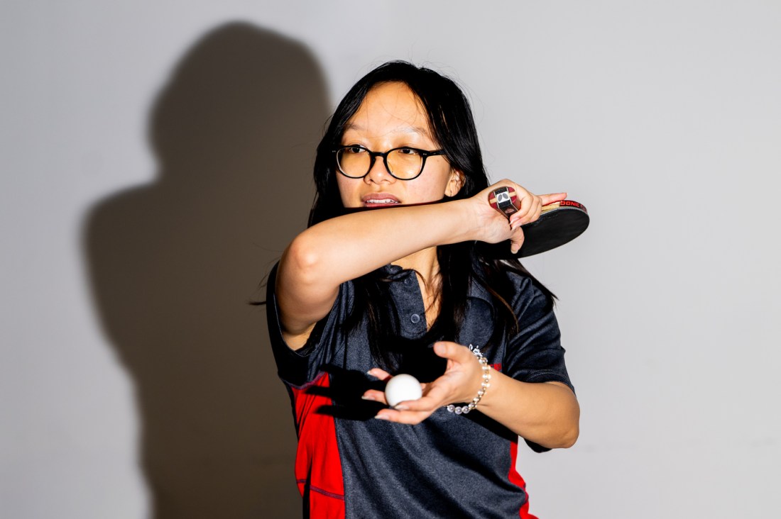 Cherie Ma gets ready to serve, holding a table tennis paddle in one hand and the ball in another.
