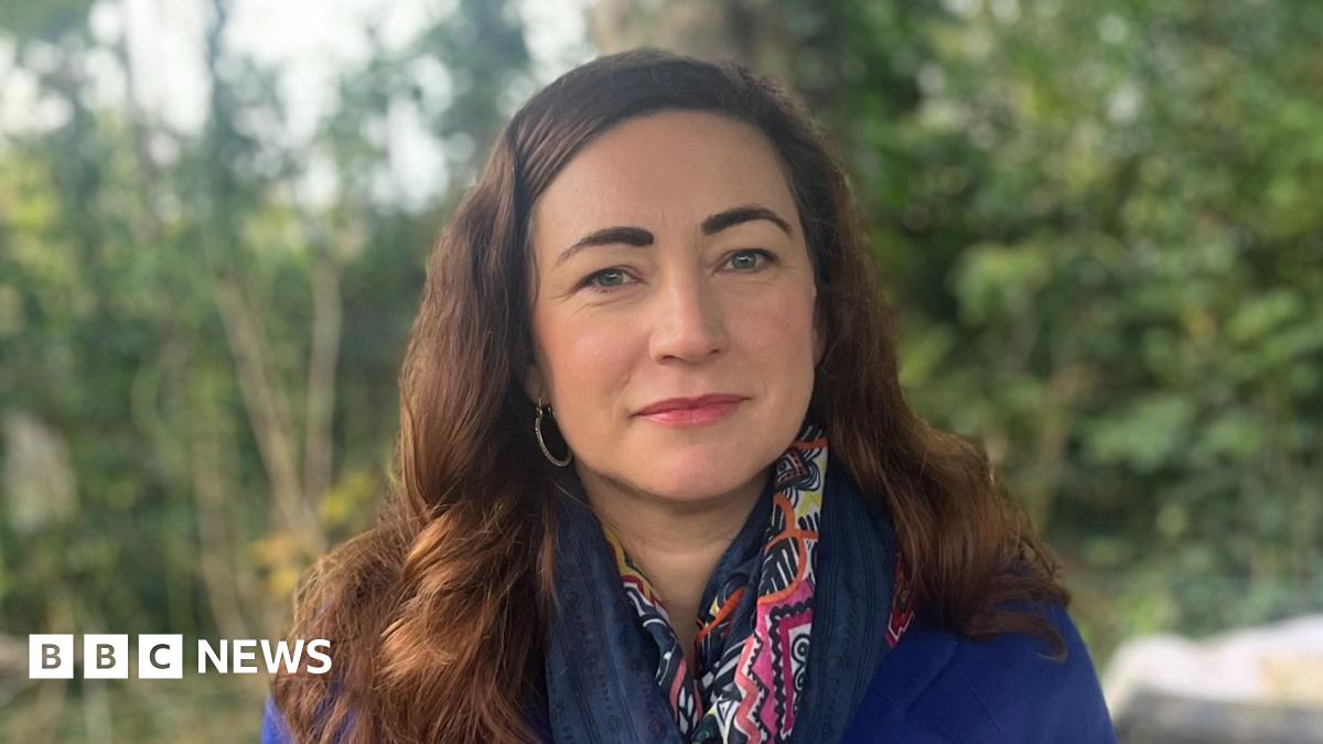 A man wearing a blue-checked shirt with his face buried in his hands