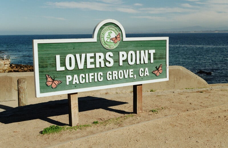 A green sign with butterflies reads "Lovers Point, Pacific Grove, CA" by the ocean, with blue water and sky in the background.