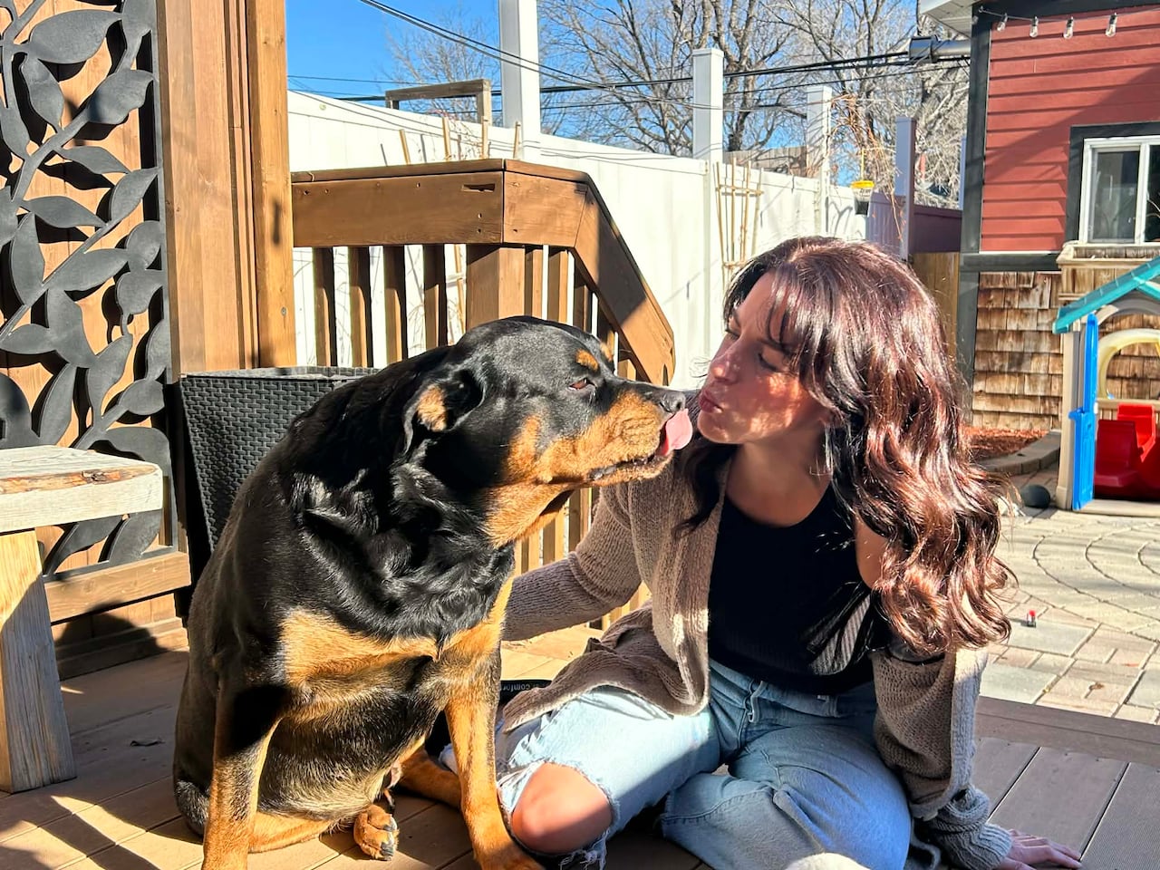 A woman kisses her dog on a deck