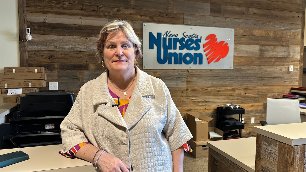 A woman is shown in a beige jacket looking at the camera with the Nova Scotia Nurses' Union logo on the wall behind.