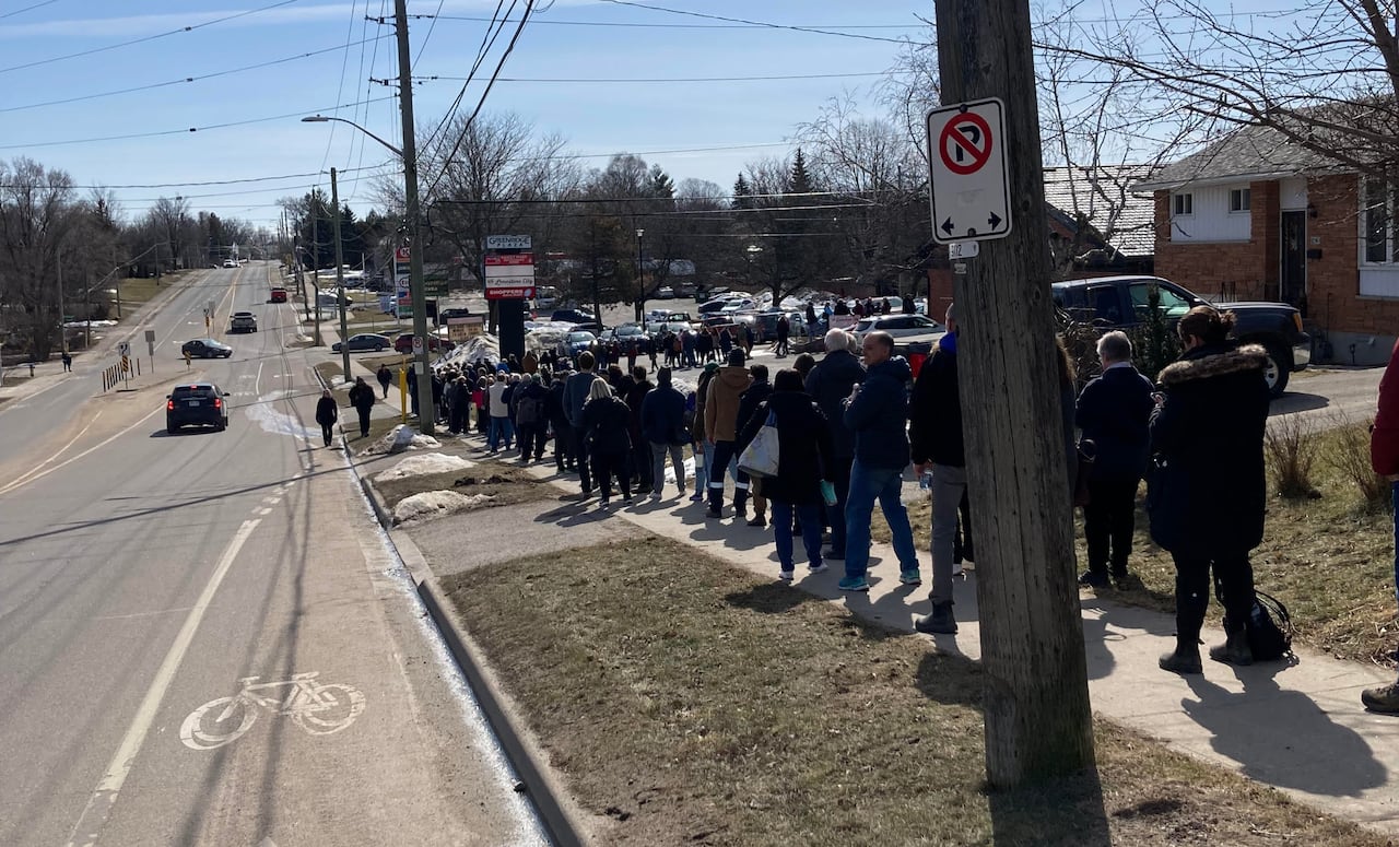 A people lining up outside on a sidewalk. 