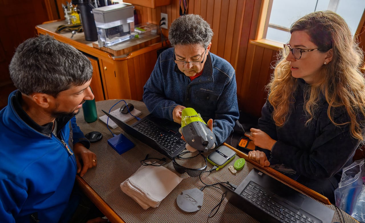 Three people look at a device on a boat.