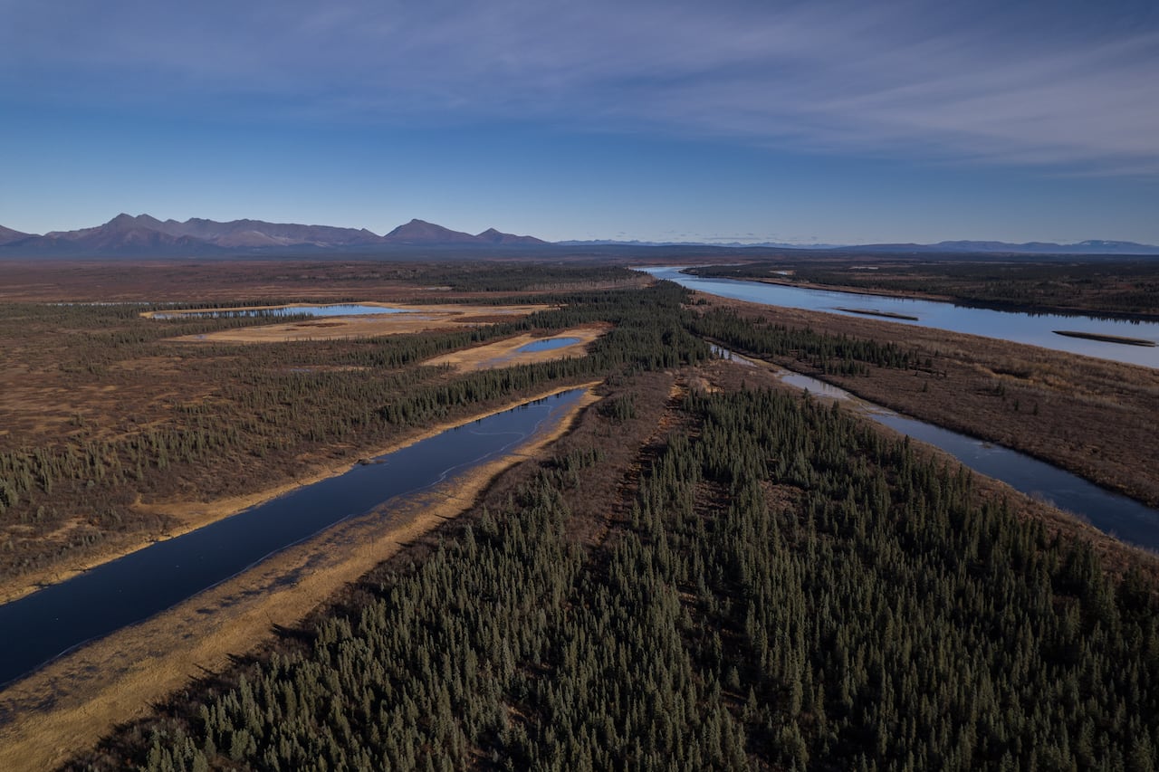 A wide view of tundra and a river, with mountains in the distance.
