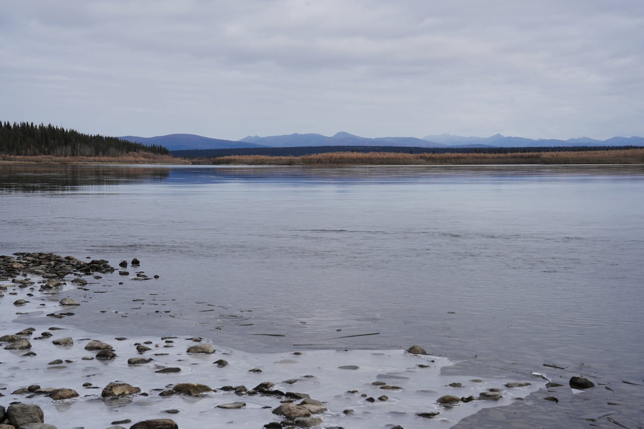 Ice forms along the banks of a wide river, with mountains visible in the distance.