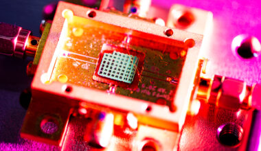 Close up of a belt-buckle-sized sensor with a computer chip at its center, the surrounding sensor is gold and the table it rests on is pink.