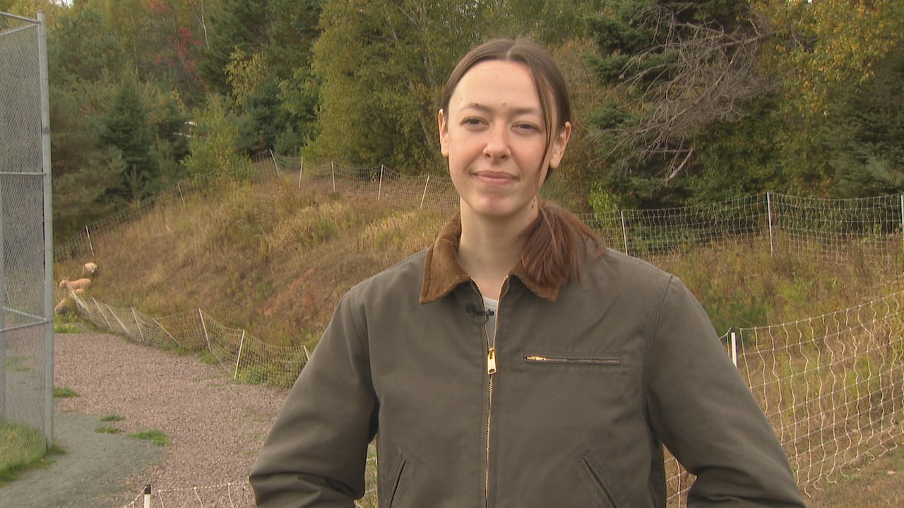 A woman in a green work jacket stands outside on a wooded hill