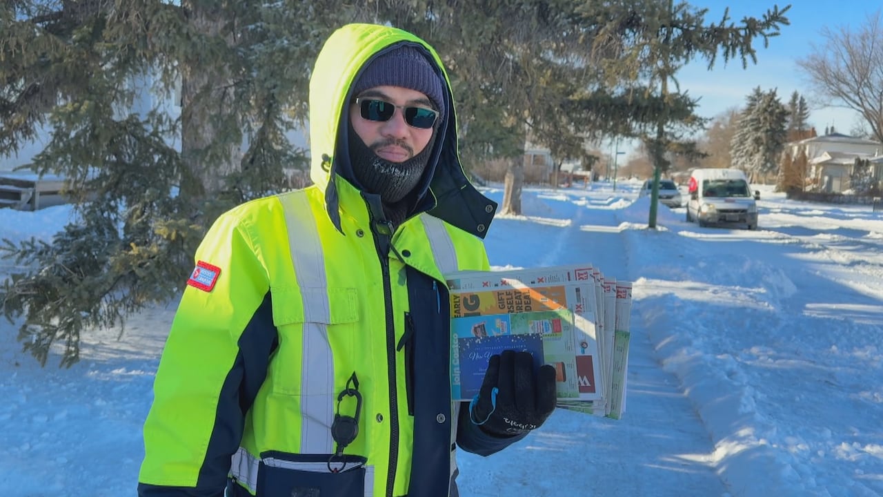 A postal worker in a yellow jacket holds papers.