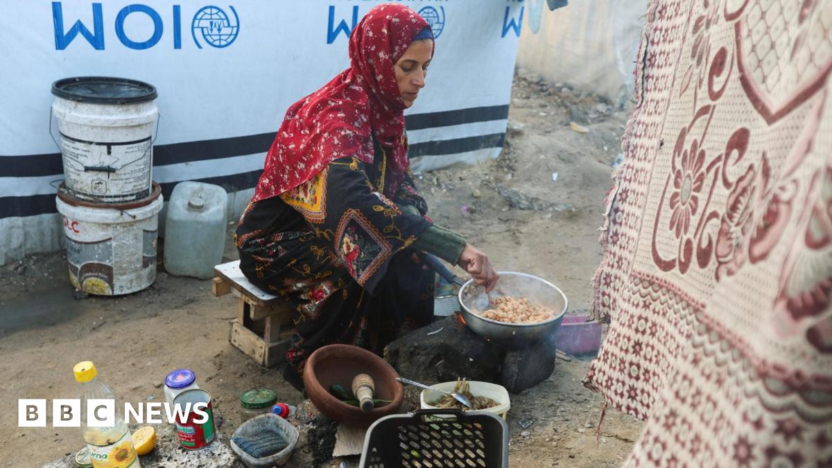 Displaced Palestinian woman Hanan Abu Taibah cooks food on a fire outside her  tent in Khan Younis, southern Gaza (18 December 2025)
