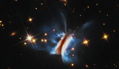 Near the center is an object that resembles an edge-on view of a hamburger. There is a diagonal dark strip (the meat patty) of dust, running from 1 o'clock to 7 o'clock, that obscures a central star. Curving away from either side of the dark strip are glowing white clouds (the buns) where dust is reflecting starlight. Bright blue finger-like wisps of material extend far above and below the dark center plane. A few dozen stars, some with four diffraction spikes, are scattered on the black background of space.