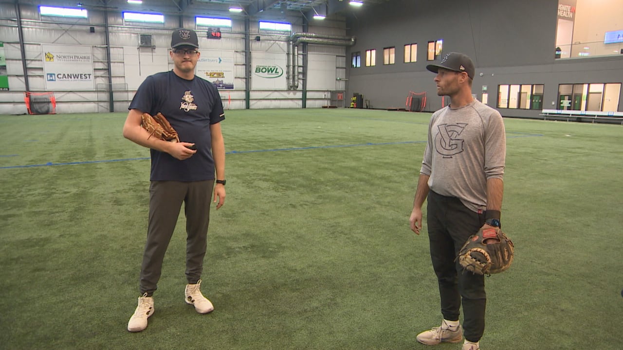 Two baseball players talk at an indoor facility.