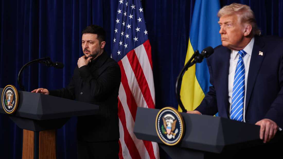 Ukrainian President Volodymyr Zelensky listens as President Trump speaks during a press conference on Dec. 28 in Palm Beach, Florida. Both men stand behind their own podiums with an American and a Ukrainian flag behind them.