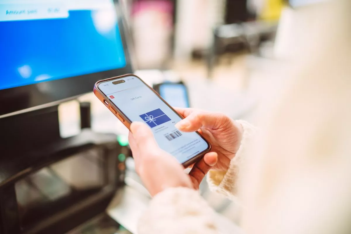 Close-up of a shopper using a digital gift card on a smart phone at a self-checkout station in supermarket.  The image highlights the seamless convenience of mobile payment technology, showcasing cashless transactions and the digital consumer lifestyle. Concepts of digital wallet, contactless shopping, and e-gifting.,