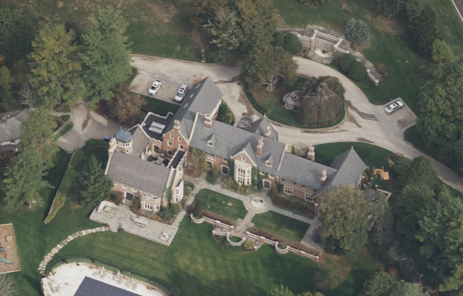 Aerial view of a large mansion surrounded by landscaped gardens and a circular driveway.