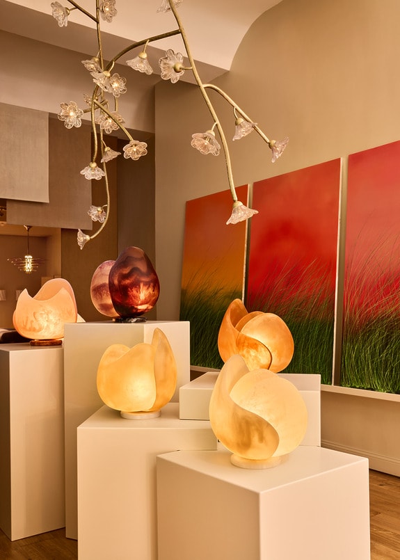 Artistic lighting display on white pedestals with flower-like ceiling lights and red-green artwork in the background.