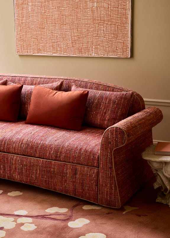 Red patterned sofa with orange cushions in a cozy living room with abstract art hanging on the wall.