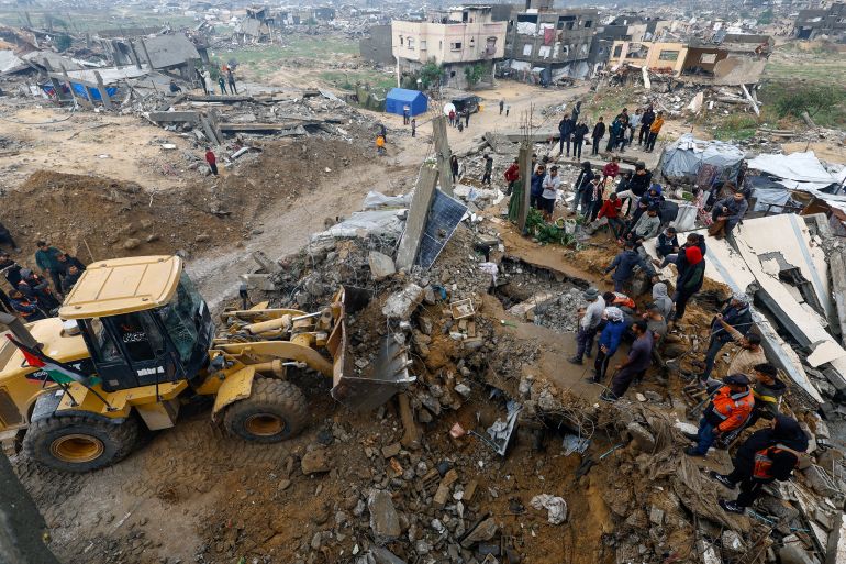 Heavy machinery operates as Palestinians gather on a pile of rubble amid a search for victims in a destroyed house that collapsed amid heavy rains, in Beit Lahia, in the northern Gaza Strip, December 12, 2025. [Mahmoud Issa/Reuters]