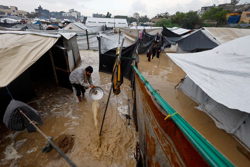 A displaced Palestinian man clears muddy water in a flooded tent camp on a rainy day in Nuseirat, central Gaza Strip, December 12, 2025.