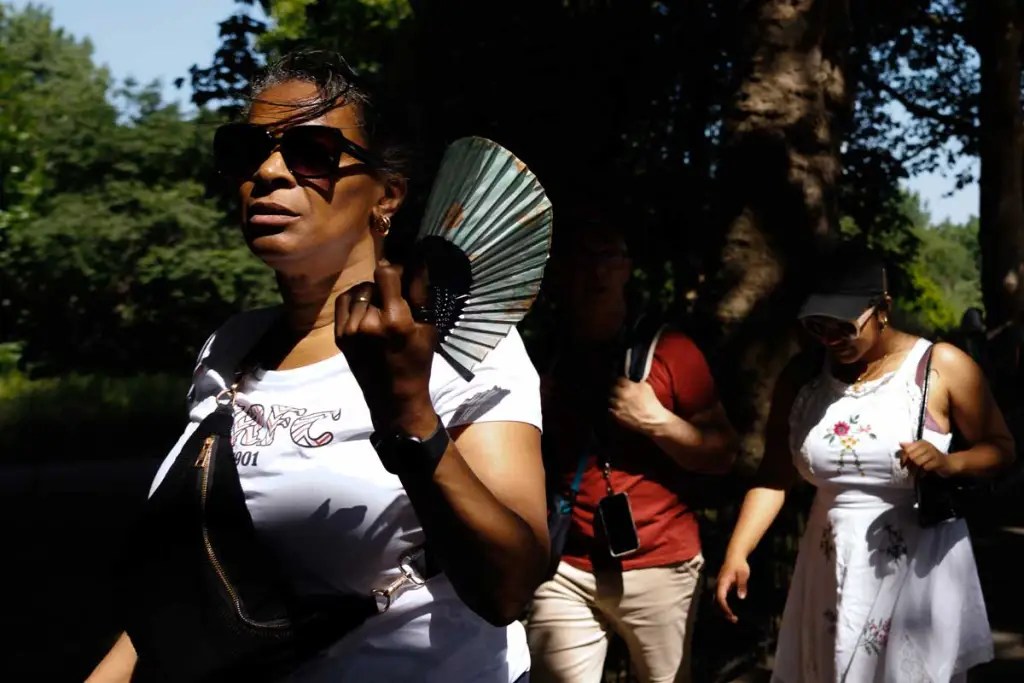 A woman fans herself as she walks through a park