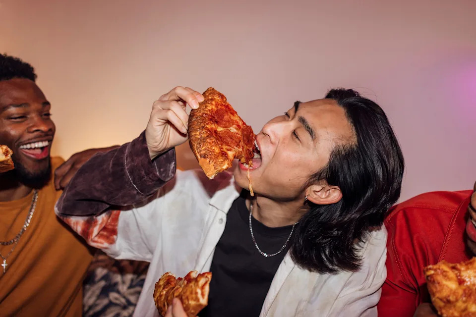 Person joyfully eating a slice of pizza with friends, enjoying a casual gathering