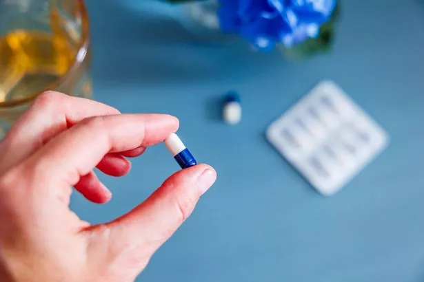 Top view of a woman's hand holding a pill against a table with medicine on it