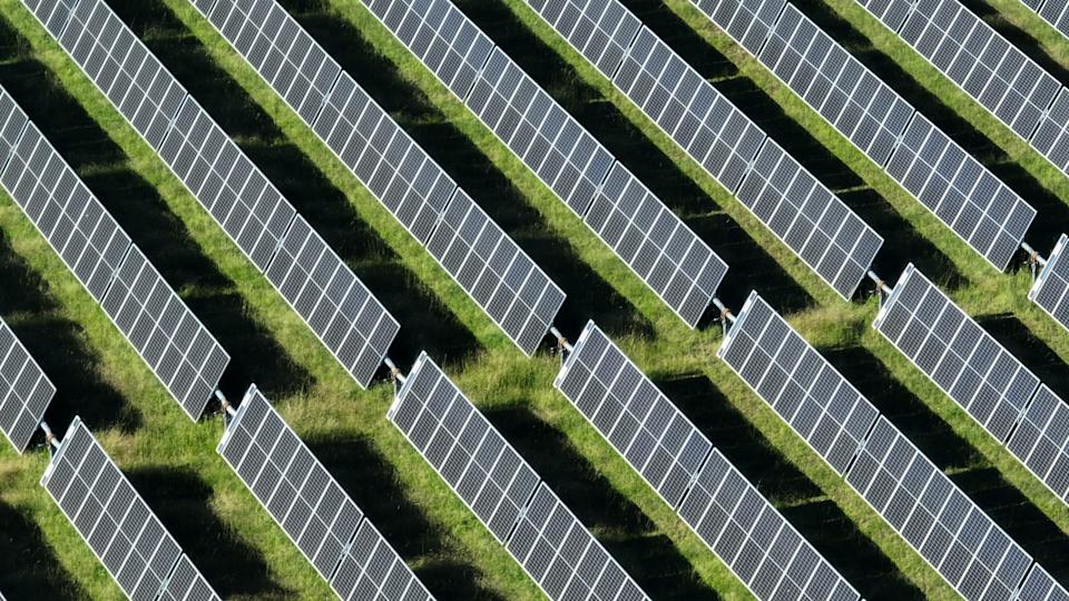 This stunning aerial view captures an  array of solar panels arranged in neat, parallel rows across the landscape. From above, the panels shimmer under the bright sunlight, creating a striking contrast against the natural terrain below. The organized rows of solar panels stretch across acres of land, symbolizing the growing global shift toward renewable energy. The grid-like pattern highlights the efficiency and scale of modern solar farms, contributing to sustainable energy production.This high-resolution image showcases the incredible reach and potential of solar power as a clean, renewable energy source. Whether situated in rural fields, expansive deserts, or atop rooftops, these solar panels represent a major step toward reducing carbon footprints and combating climate change. The solar farm's orderly rows and reflective surfaces create a visually appealing scene, demonstrating both technological innovation and environmental responsibility.