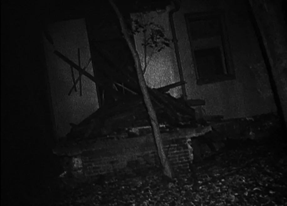 Old, abandoned house at night with debris and a tree in the foreground