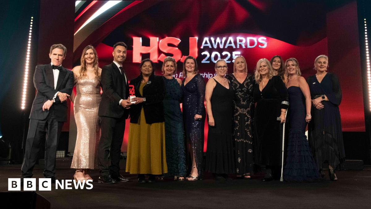 A group of men and women stood on stage accepting an award, dressed in black tie