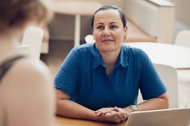 Kirstin Hunter wears a blue dress and sits at a table with a laptop in front of her.
