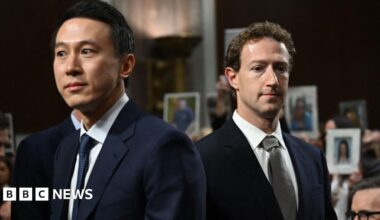 A brown NC500 sign post which says it is 27 miles to Ullapool next to a country road with hills in the background.