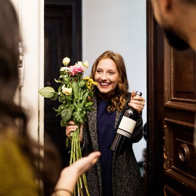 Woman holding bouquet and wine bottle while visiting friends