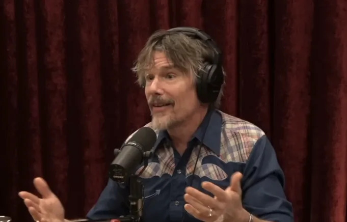 A person with headphones speaks animatedly into a microphone during a podcast, wearing a casual western-style shirt