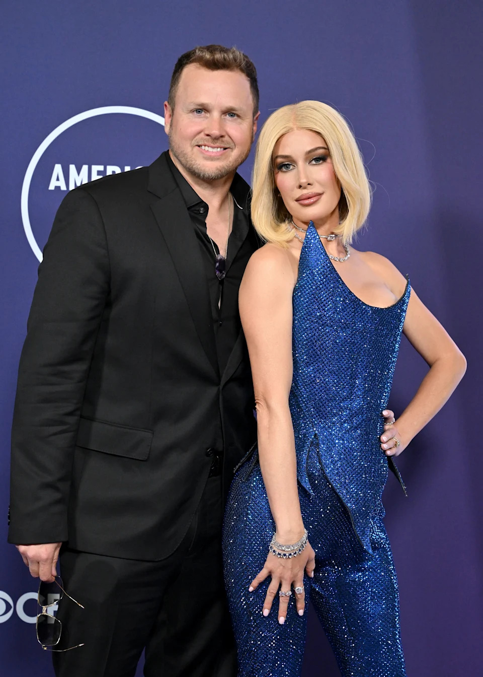 A man in a black suit and a woman in a shimmering blue dress pose together at a formal event