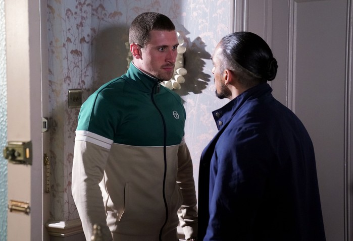 Harry, in a green and beige tracksuit top, confronts Ravi - who is wearing a navy blue jacket - in a scene from EastEnders