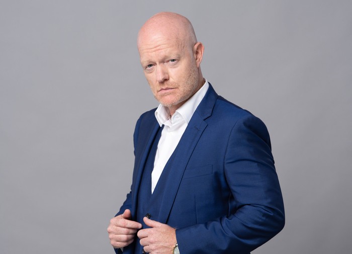 Jake Wood poses in a navy suit as Max Branning against a grey background in a promo photo for EastEnders.