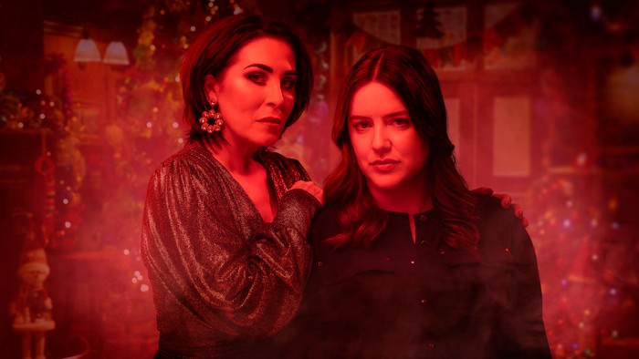 542868,TITLE:Eastenders Kat Moon placing her hand on Zoe Slater's shoulder. The trio are tinted in red, with the Queen Vic's Christmas decorations behind them in EastEnders