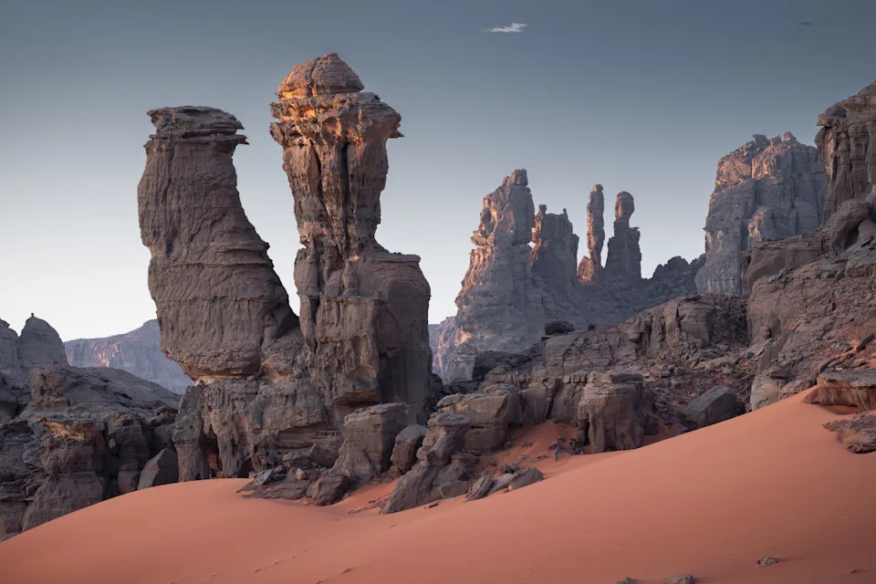 A series of dark sculptures rise up from the reddish sands of central Sahara. Tassili N'Ajjer National Park, Argelia.