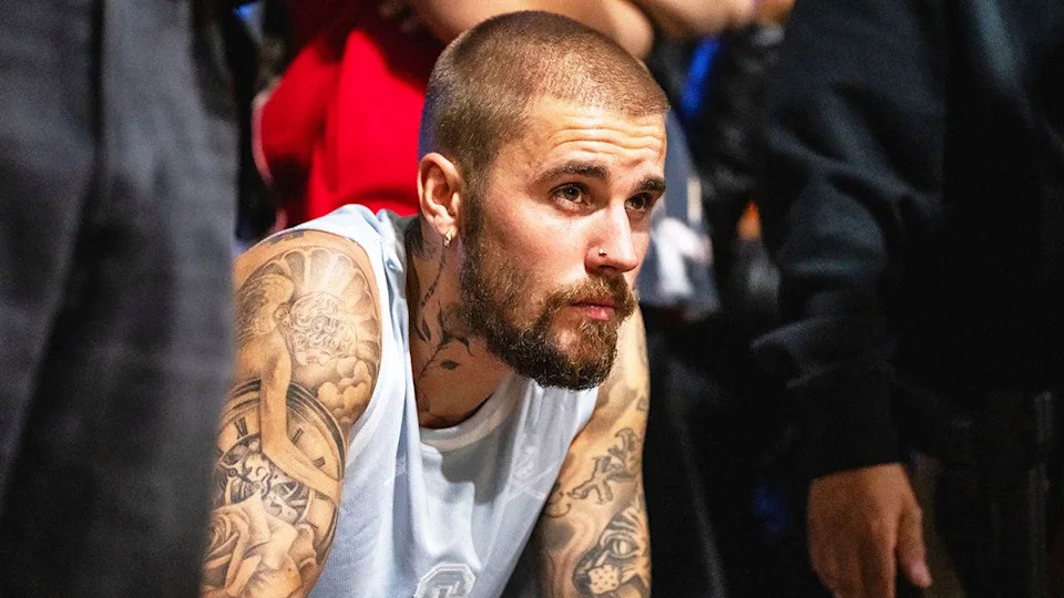 A close-up of Justin Bieber wearing a sleeveless white shirt looking reflective.