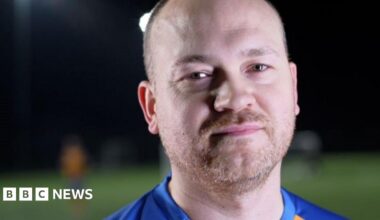 Freddie Kizis-Stevens is wearing a yellow and blue football shirt, with a Sands United crest. He is standing on a football pitch.