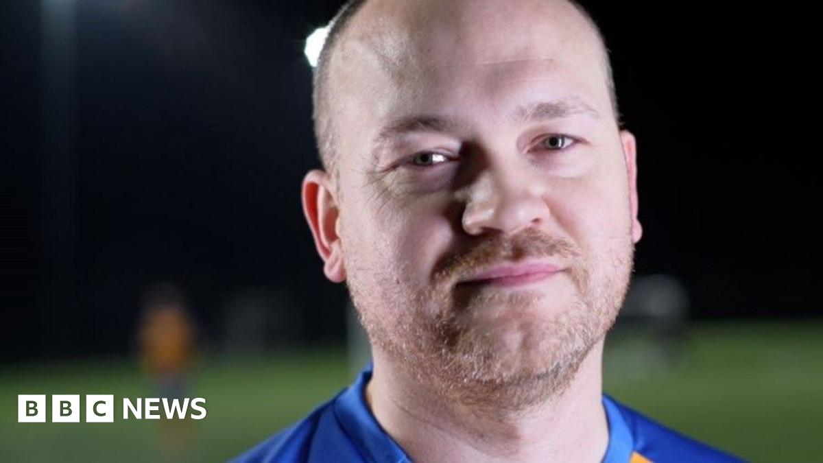 Freddie Kizis-Stevens is wearing a yellow and blue football shirt, with a Sands United crest. He is standing on a football pitch.