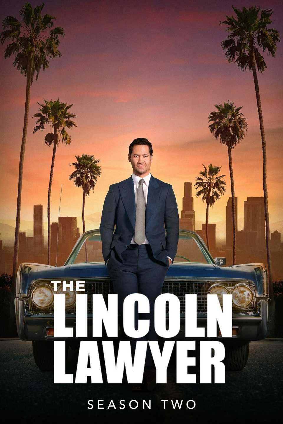 Mickey Haller (Manuel Garcia-Rulfo) is leaning against a car on a street lined with palm trees on the poster for The Lincoln Lawyer.