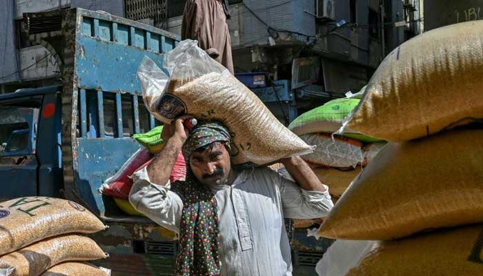A labourer carrying a sack of pulses from a truck at a wholesale market in Karachi on September 26, 2024. — AFP