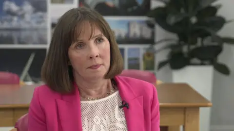 A woman in a pink suit, with a brown bob and gold necklace