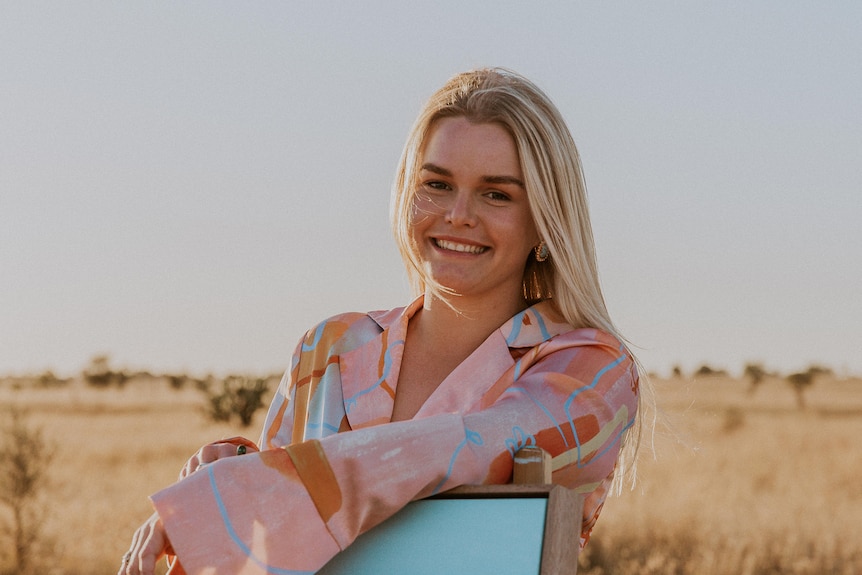 Zarabella poses for a professional photo while leaning on one of her paintings in a field.  