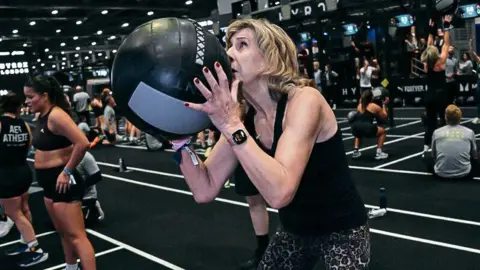 Hyrox Mrs Reid holds a weighted medicine ball that she is preparing to throw upwards as part of a Hyrox event. 